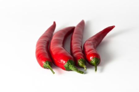 four chili peppers with stems on a white background.