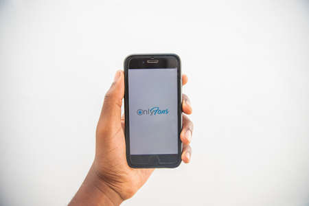 Smartphone with the OnlyFans logo held in the hand by a person. OnlyFans is a popular content subscription service. Iphone isolated on white background.のeditorial素材
