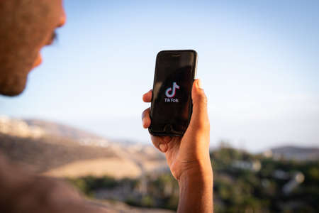 A boy holds a smartphone with the TikTok logo, it's a very popular app and a video-focused social...