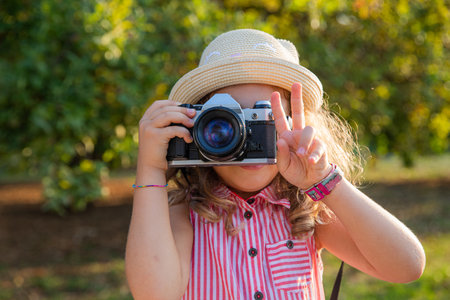A little girl with a camera takes pictures and makes the V sign with her fingers, photographer...