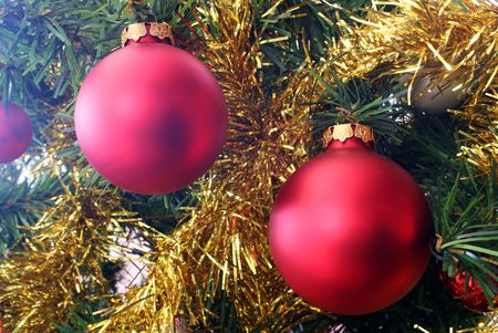 A close up of two red christmas bauble decoratopns and gold tinsel hanging on a christmas treeの写真素材