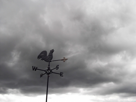 Dark clouds behind a weather vane indicating bad weather and wind directionの写真素材