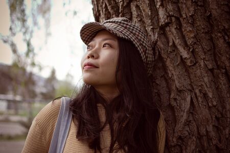 Attractive Asian Female College Student Looking Into The Distance While Leaning Against A Tree...
