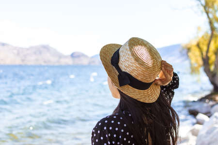 Young woman wearing a straw hat gazing out onto Okanagan Lake in British Columbia, Canada....