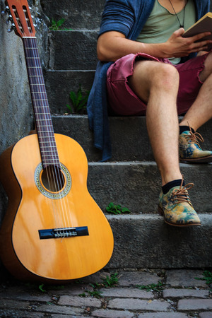 Street artist sits with his guitar on a staircase and reads a book.の写真素材