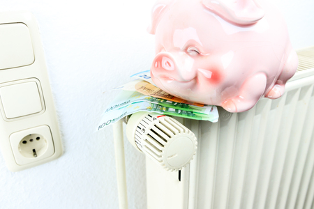 Money and piggy bank on a radiator symbolizes the expensive heating costs.の写真素材