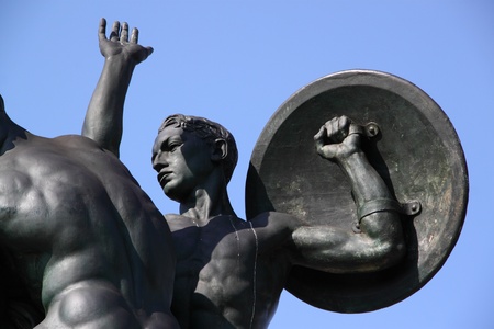 A bronze statue of a young soldier with a shield, on a blue sky backgroundの写真素材