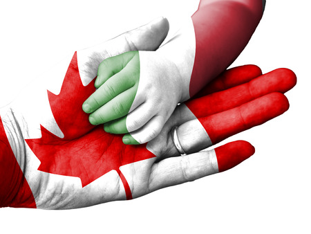 Canada flag overlaid the hand of an adult man holding a baby hand with the flag of Italy overprinted. Conceptual image for help, aid, assistance, rescue. Isolated on white backgroundの写真素材