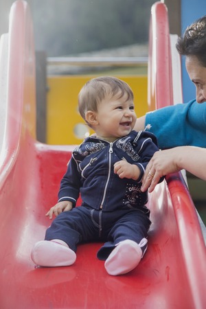 Portrait of smiling lovely one year old baby on plastic slide looking at motherの写真素材