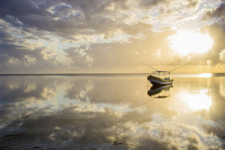 Sailing boat on reflected water surface under cloudy sky at dawn