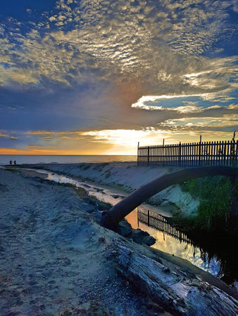 Beach with small river reaching the sea with cloudy sky.の写真素材
