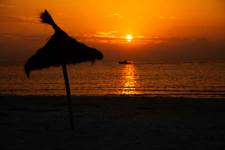 Parasol out of straw at tropical beach in front of the ocean with a boat while sundown perfect...