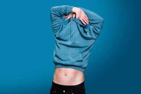 pulling blue sweatshirt over head and hiding face while making naked stomach visible