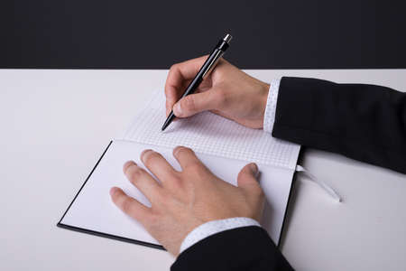Hands of a businessman making notes in his notebook from side view