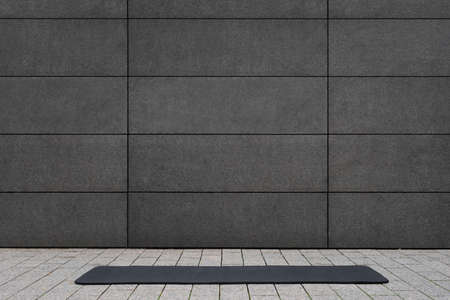 empty and blank foldable black yoga mat on gray sidewalk near empty street outdoor in front of...