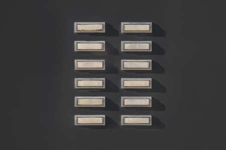empty name tags of multiple door bell buttons on front of minimalistic black wall of an apartment housingの写真素材