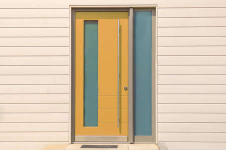yellow front door on wooden wall with glass and long metal handle is a designer exterior of a...