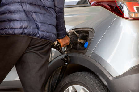 pump gas at gas station while put nozzle by hand in car hole to refuel the tank with diesel next to...