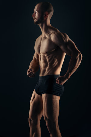 Athletic man in underwear standing on black background showing his muscles while posing as bodybuilderの写真素材