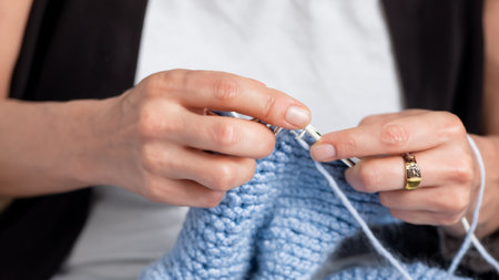 Delicate female hands skillfully weave and loop blue yarn as they create a beautiful knitted masterpiece. The rhythmic motions bring warmth and comfort, showcasing the timeless artistry of knittingの素材