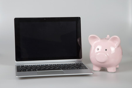 Pink piggy bank standing next to open laptopの写真素材