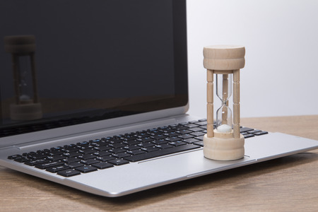 Sand running through an egg timer on a laptop computer measuring passing time as it counts down to a deadline in the office or conceptual of pressure and stressの写真素材