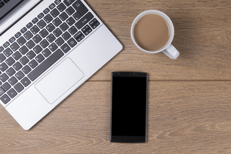 Overhead view on a business workstation on a wooden desk with an open laptop, coffee and smartphone with blank black screen and copy spaceの写真素材