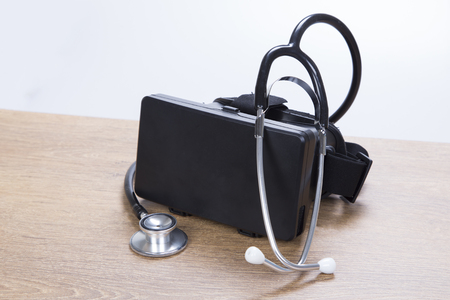 Stethoscope wound around the top on a 3d VR virtual reality headset on a wooden table in a concept of repair, maintenance and diagnosticsの写真素材