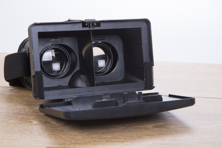 Open 3d VR virtual reality goggles or headset showing the optical lenses for creating simulated three-dimensional environments on a wooden desk in a close up viewの写真素材
