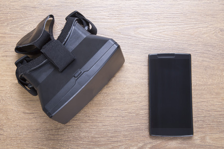 3d VR virtual reality headset with blank black smartphone lying on a wooden table or desk viewed from overheadの写真素材