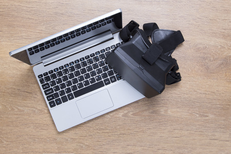 3d VR virtual reality headset on an open laptop keyboard reading for gaming on a wooden desk viewed from above with copy spaceの写真素材