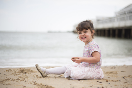Young girl sat on a beach looking at camera with a big smile on her faceの写真素材