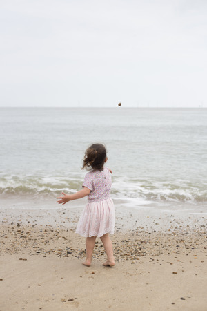 Young girl standing on a beach, throws a stone into the seaの写真素材