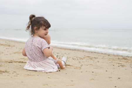Toddler sitting on a sandy beach with her dollyの写真素材