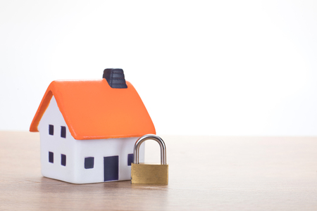 Locked brass padlock with a model house in a concept of ownership, security, insurance risk, or foreclosure by the bank with copy space alongsideの写真素材