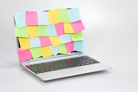 Business multitasking, ideas and organisation concept with colorful sticky notes completely covering an open laptop screen over a white backgroundの写真素材