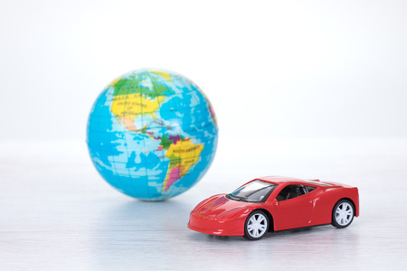 Sporty red toy motor car with a world globe in a concept of worldwide travel destinations or saving the planet through the use of eco-friendly fuels or hybridisationの写真素材