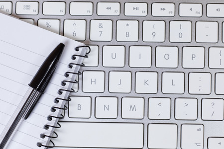Blank notepad and pen resting on top of computer keyboardの写真素材