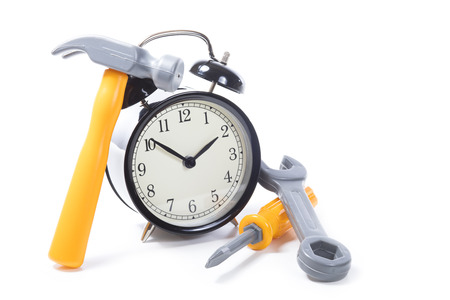 Still life of a round retro alarm clock with tools including a hammer, spanner and screwdriver in a DIY and home improvements concept of deadlines and a scheduleの写真素材