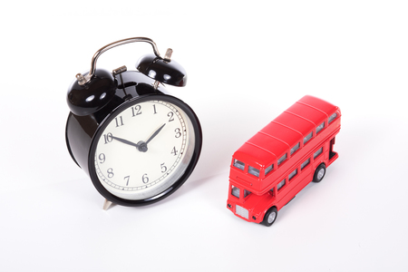 Classic black alarm clock near red Britain double-decker bus toy, viewed from high angle and isolated on white backgroundの写真素材