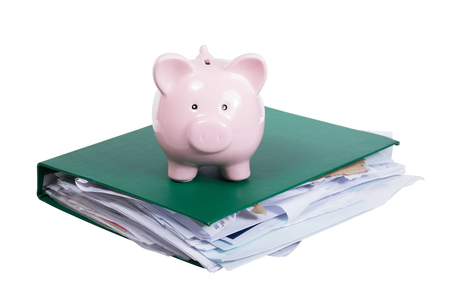 Large bulging office binder full of paperwork with small pink piggy bank on top isolated on white in a conceptual imageの写真素材