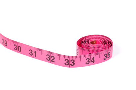 Pink measuring tape roll marked in inches with one end going outside the frame, close-up isolated on white background with copy spaceの写真素材