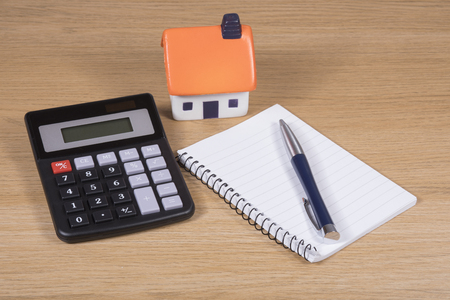 Model house, calculator and notebook with pen on a wooden table in a concept of costs and planning for purchase, maintenance and home improvementsの写真素材