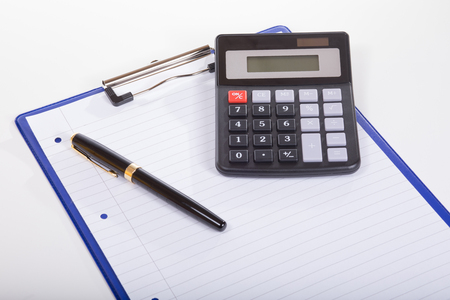 Calculator, white lined paper in tablet and pen, in concept of planning. Isolated on white, close-up view from high angleの写真素材