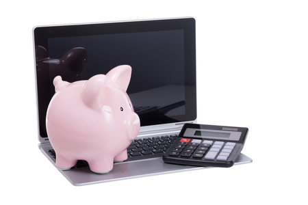 Calculator and piggy bank on an pen laptop resting on the keyboard in a conceptual financial savings and investment image isolated on whiteの写真素材