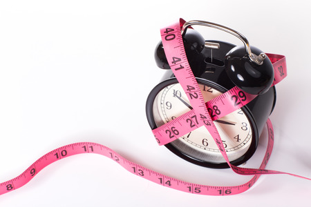 Classic black alarm clock entangled with measuring tape, on white surface with copy space, viewed from high angleの写真素材
