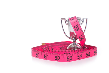 Red measuring tape marked in inches coiled around small silver sports cup, front view isolated on white background with copy spaceの写真素材