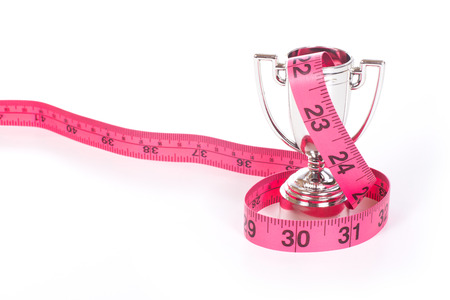 Red measuring tape entangled over small silver sports cup, isolated on white background with copy...