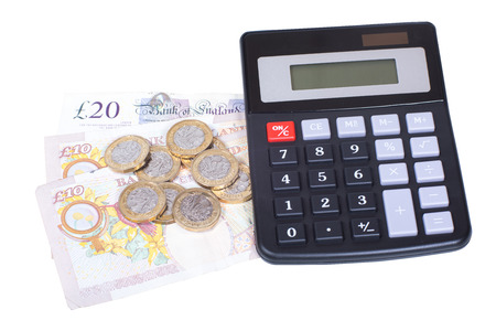 Pile of cash with pound sterling coins and banknotes together with a calculator on white in a financial or accounting conceptの写真素材