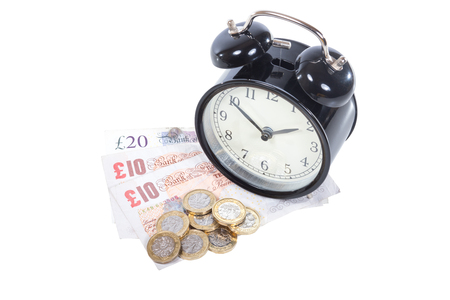 Conceptual financial concept with a pile of UK money including notes and coins and alarm clock isolated on whiteの写真素材